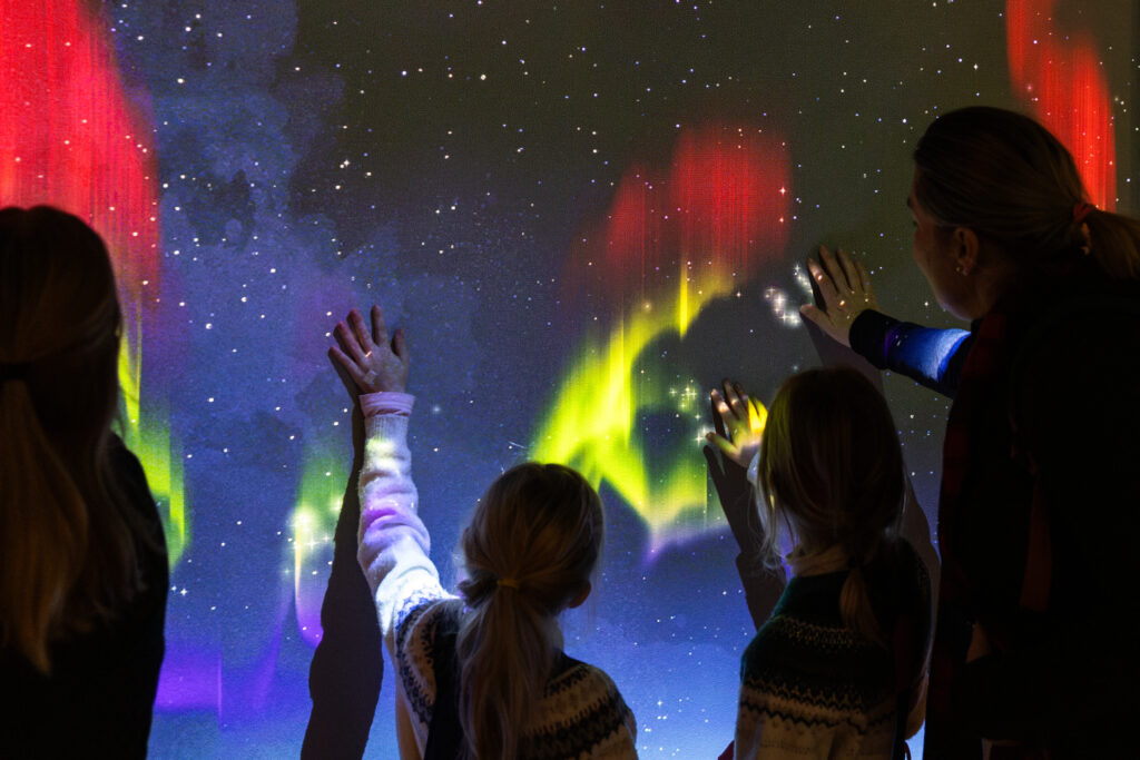 Lapset maalavat revontulia käsillään seinälle.