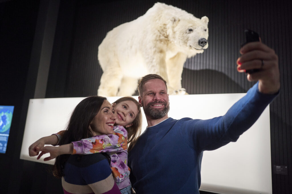Perhe ottaa selfietä, taustalla täytetty jääkarhu.