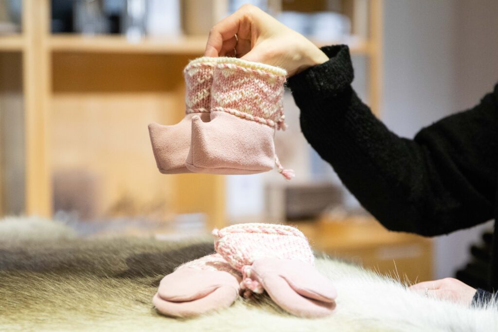 Kädessä vaaleanpunaiset lapsen poronnahkatossut.