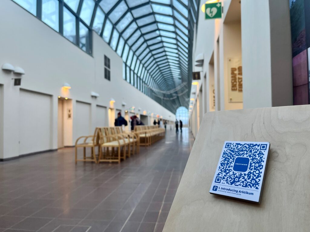 Taustalla Arktikumin lasiputki ja edessä telineessä QR-koodi.