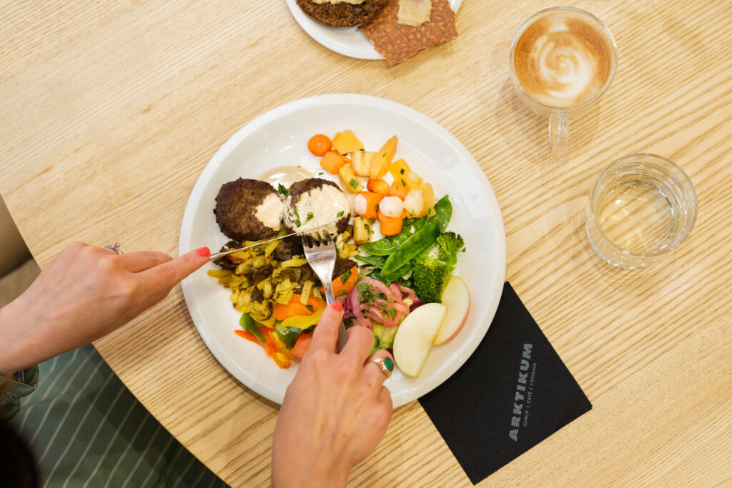 Kuvassa on lautanen, jossa lounasta. Kuvassa näkyy myös kaksi kättä.