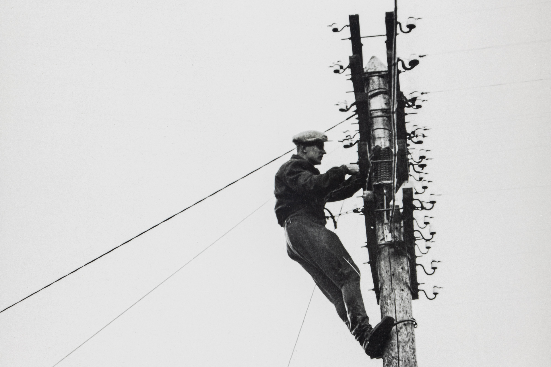 Mustavalkoinen kuva, jossa mies kiipeää puhelintolppaa pitkin